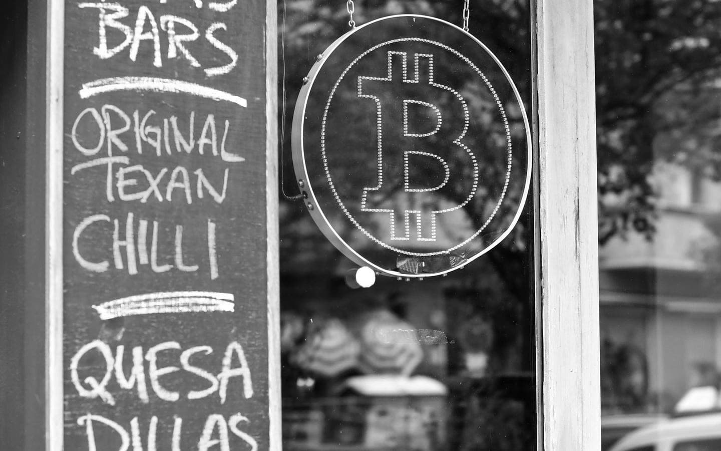 A neon Bitcoin sign in a shop window beside a chalkboard menu
